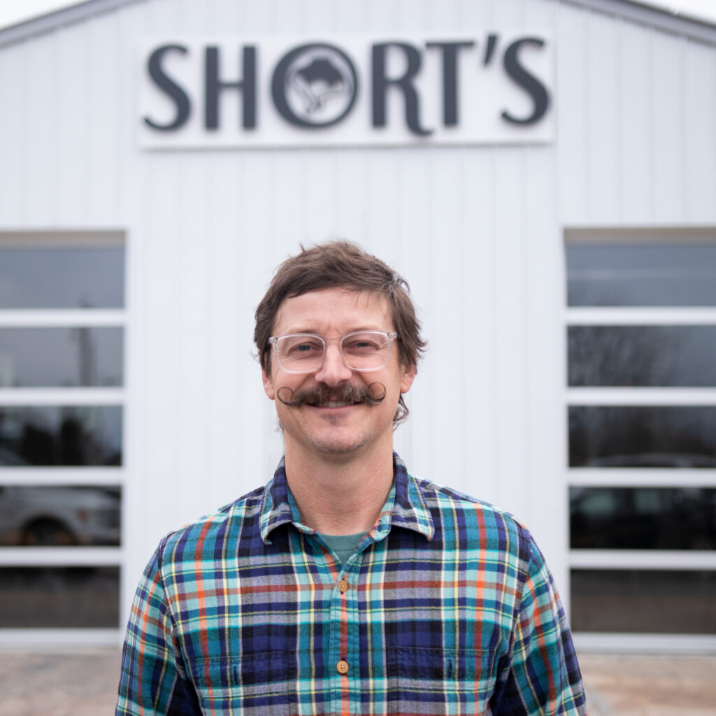Joe Short, with a curly mustache and twinkle in his eye, stands in front of the Short's Elk Rapids location