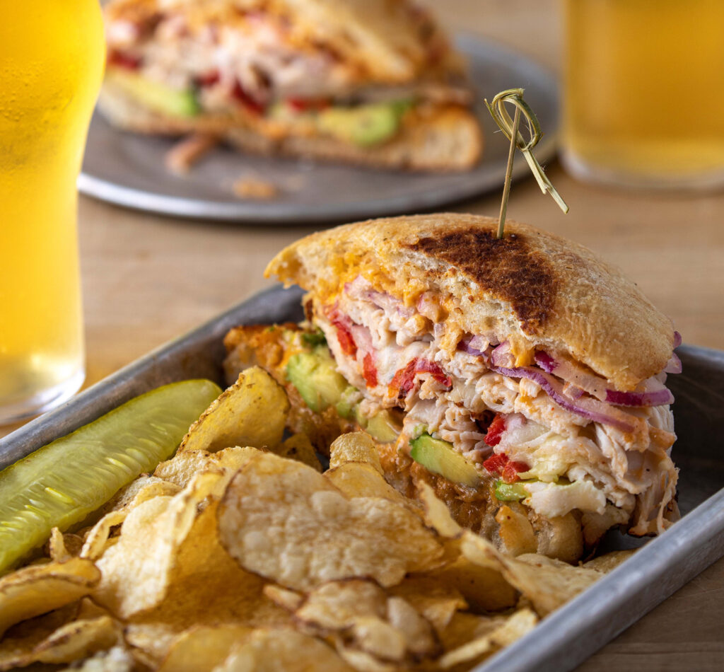 Mouthwatering turkey sandwich with avocado, chips, and ice cold lagers