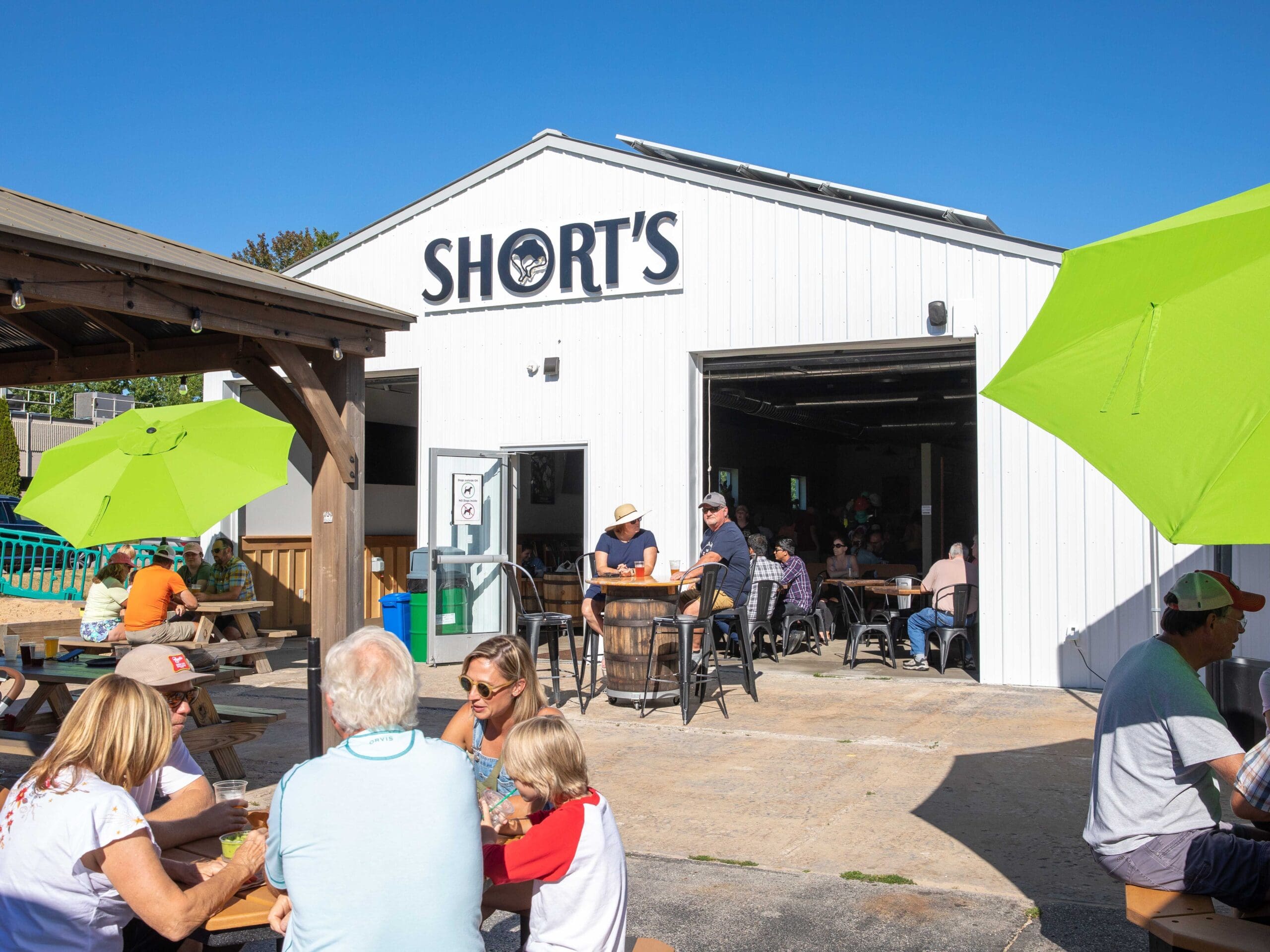 Photo of the Elk Rapids Pull Barn in summer with people sitting outside at picnic tables